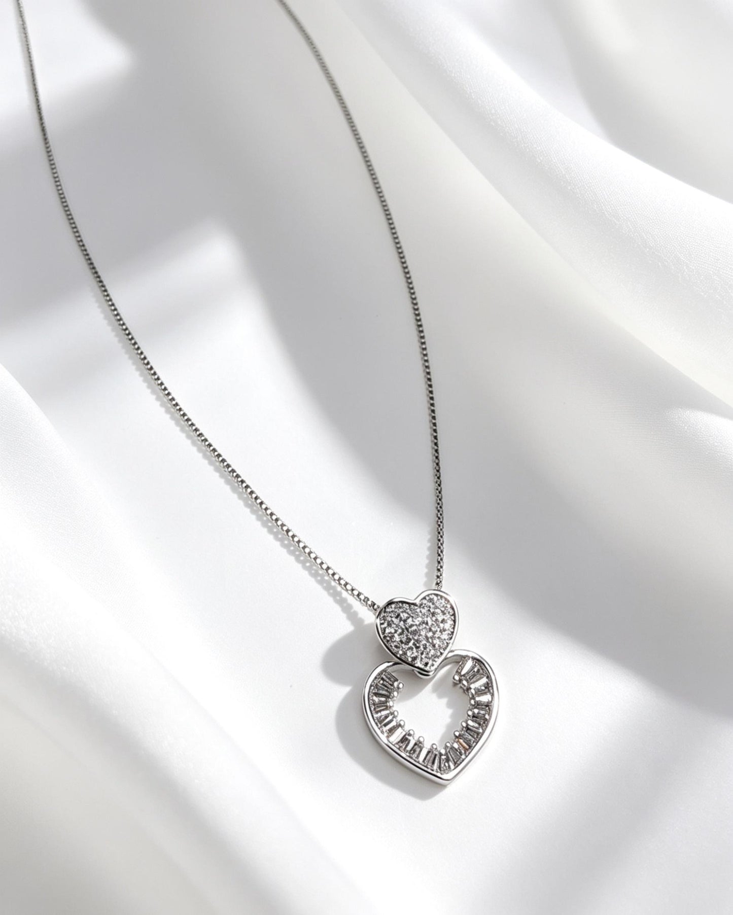 Collar con un dije doble compuesto por un corazón superior texturizado con microcirconias, que se conecta a un corazón decorado con cristales.