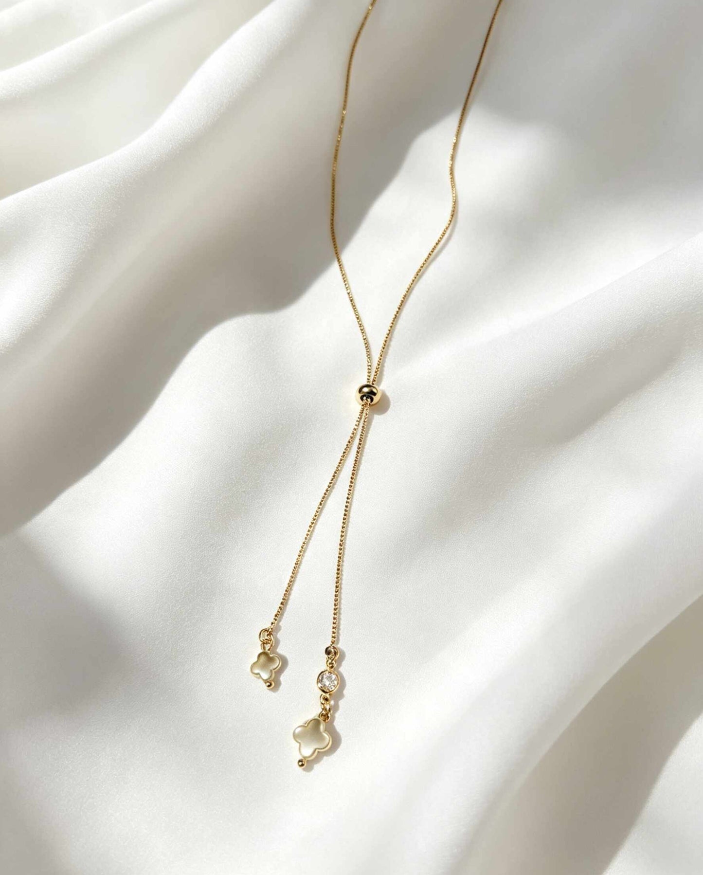 Collar ajustable estilo corbatín, con dijes de trébol de cuatro hojas confeccionados en madre perla y cuenta con un pequeño punto de luz.