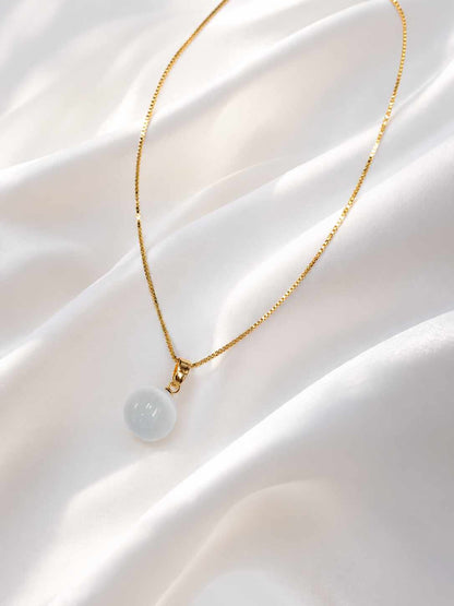 Collar delicado con un dije esférico de color blanco lechoso, montado sobre una fina cadena dorada. 