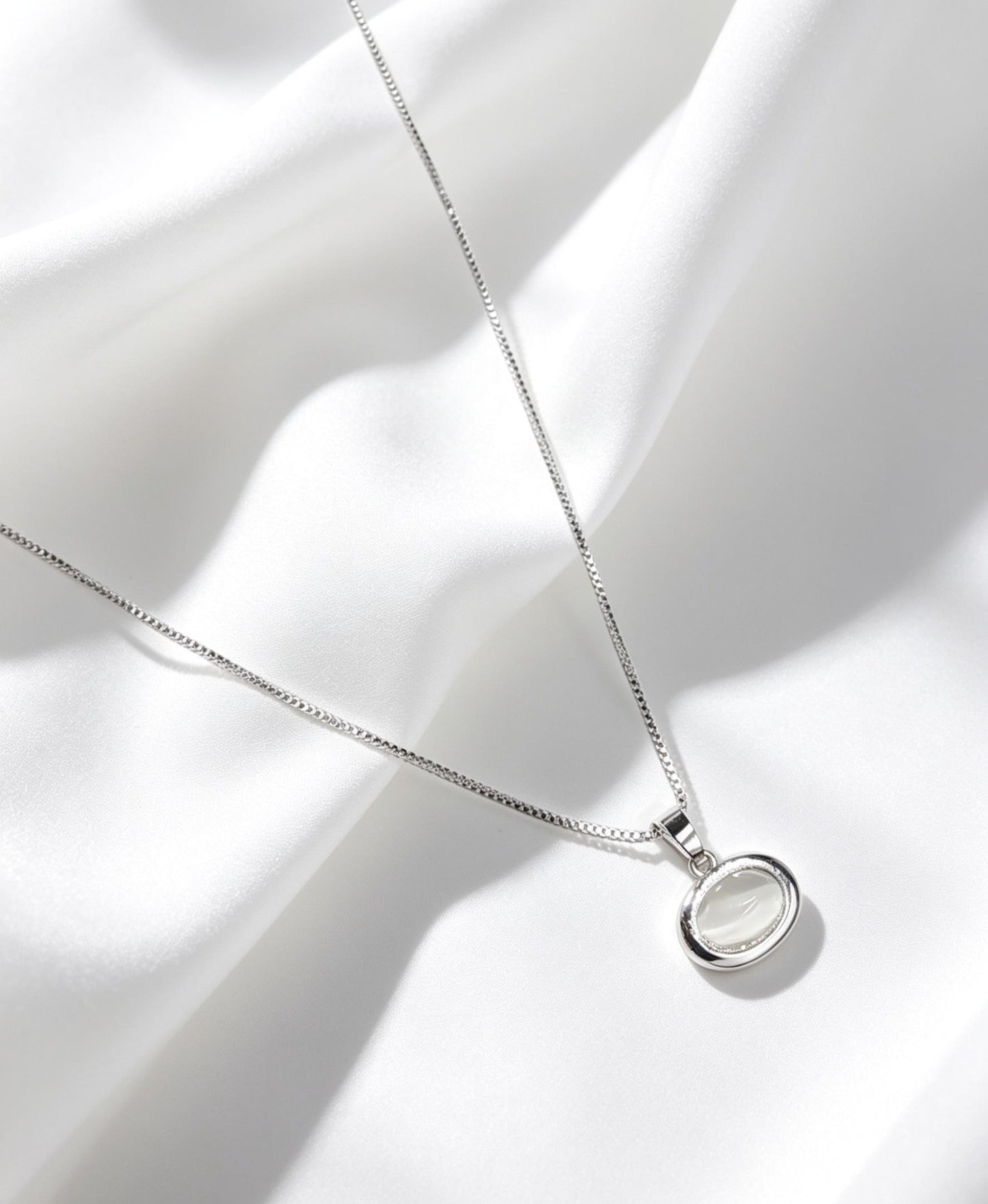 Collar con dije ovalado con una piedra semitransparente, la cual presenta un efecto óptico de destello similar a la piedra luna. 