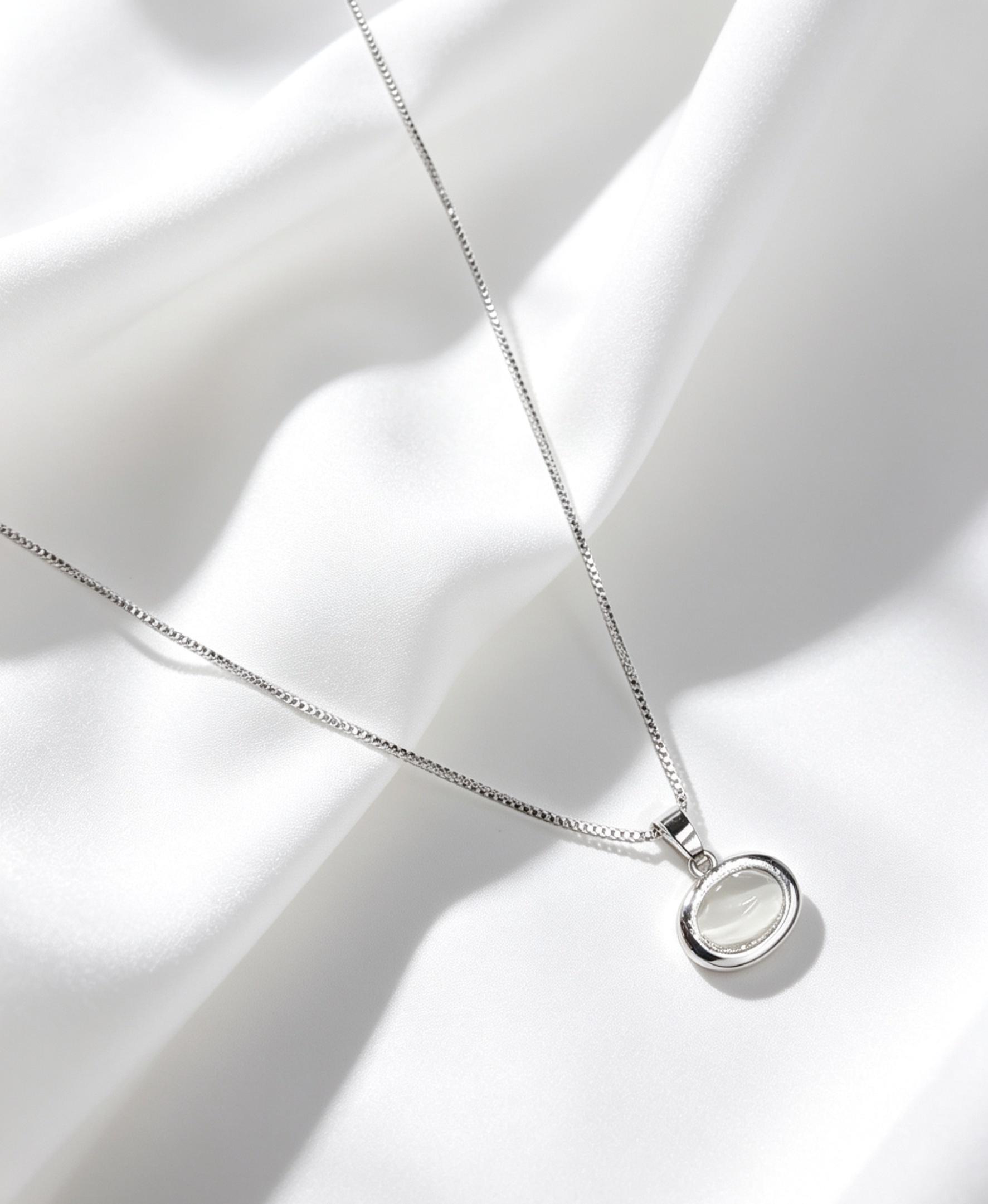 Collar con dije ovalado con una piedra semitransparente, la cual presenta un efecto óptico de destello similar a la piedra luna. 